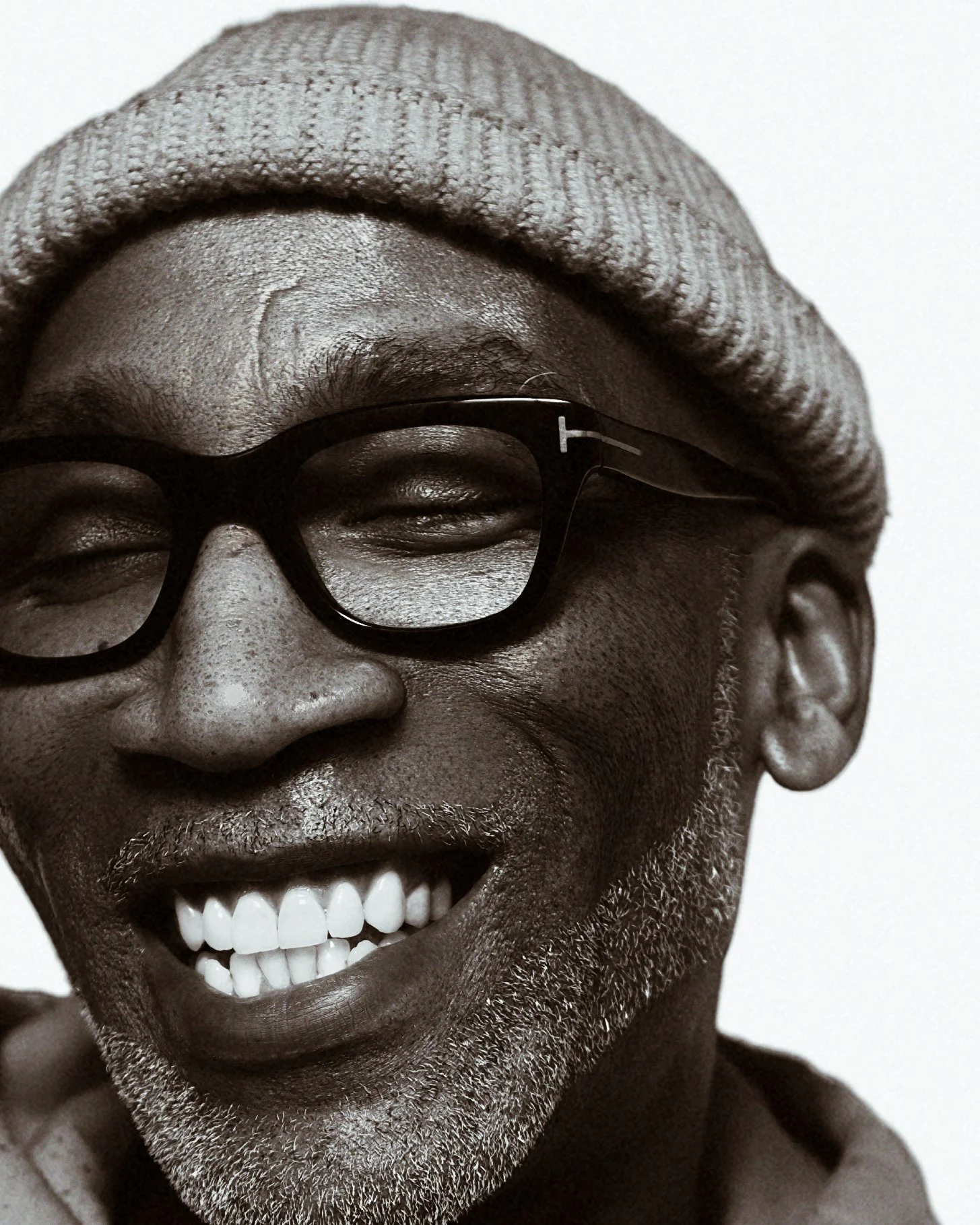 Close-up of a smiling middle-aged man with glasses, a beanie, and a beard, in black and white.