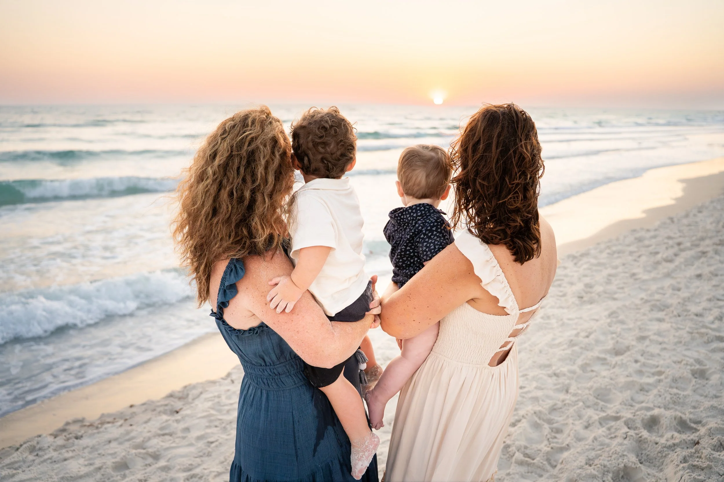 Family beach photo session at sunset in Sarasota, Florida with two mothers holding young children by the ocean, captured during golden hour by Sarasota family photographer The Coastal Boheme Photography.