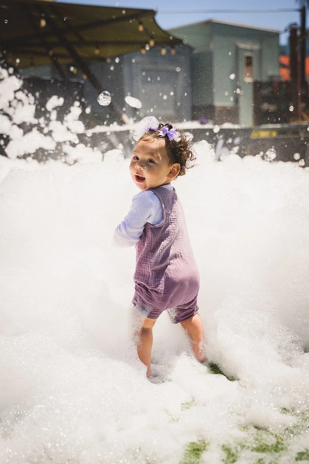 A young child playing in Oogubi Foam, with foam covering the ground and bubbles floating in the air at a Oogubi Wonderland, an Oogubi Signature Event.
