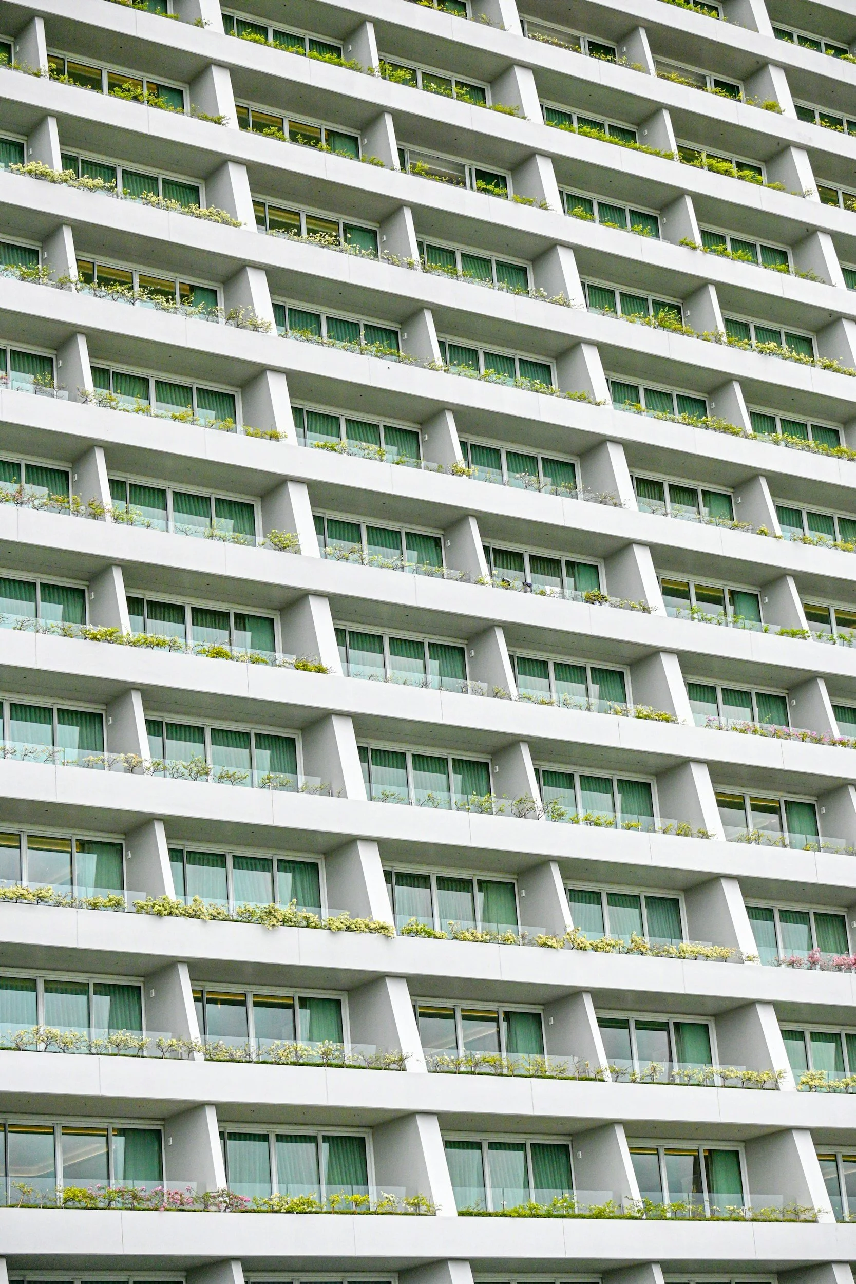 Multiple floors of a modern apartment building with protruding balconies and green plants.