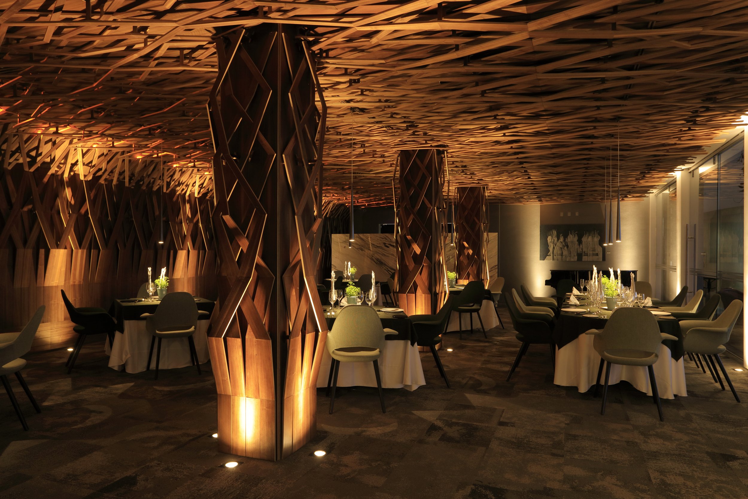 Elegant restaurant interior with modern wooden partitions, round tables with white tablecloths, and stylish chairs, illuminated by soft warm lighting.