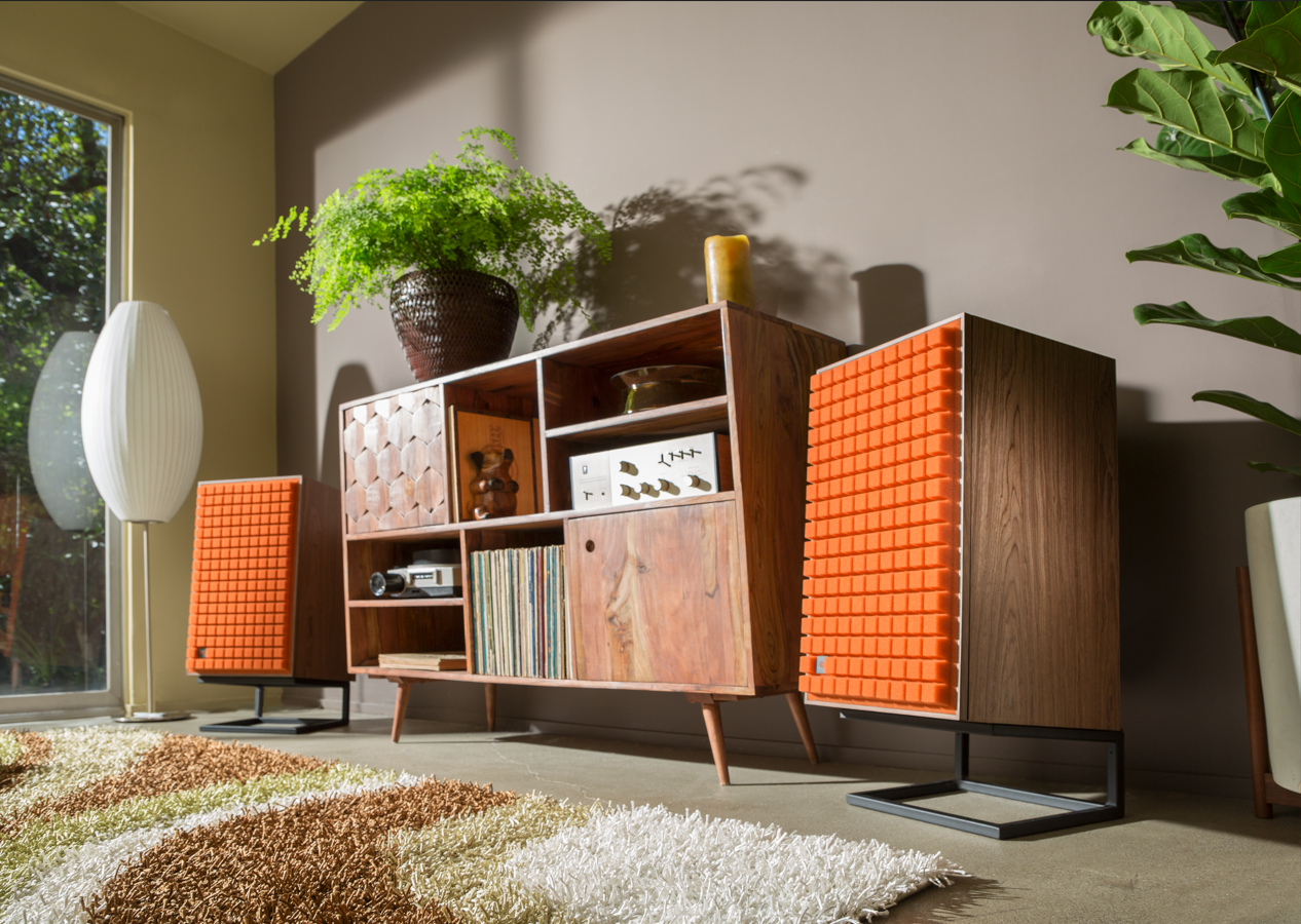 Living room with a wooden sideboard with orange speakers, greenery on top, vinyl records, a vintage camera, and decorative items, near a large window and a floor lamp, with a textured rug on the floor.