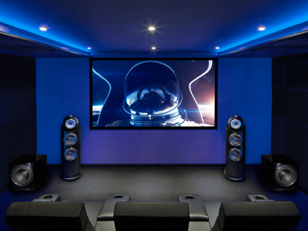 A home theater room with a large screen displaying an astronaut in space, surrounded by blue LED lighting, with black speakers and seating.