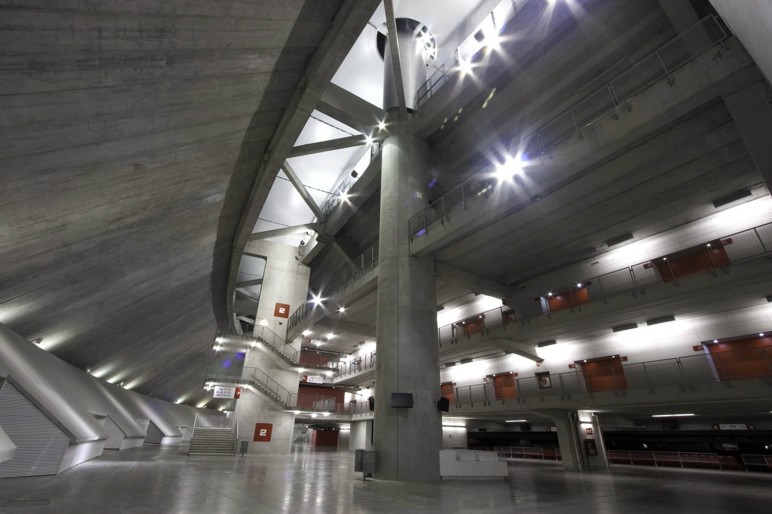 Interior of a modern multi-level parking garage with concrete walls and red doors, illuminated by bright ceiling lights.