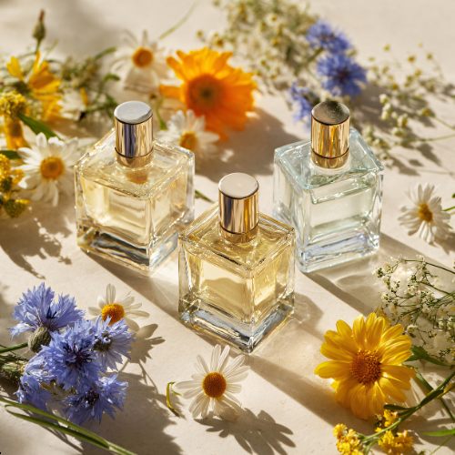 Three glass perfume bottles with silver caps surrounded by colorful wildflowers on a white surface.