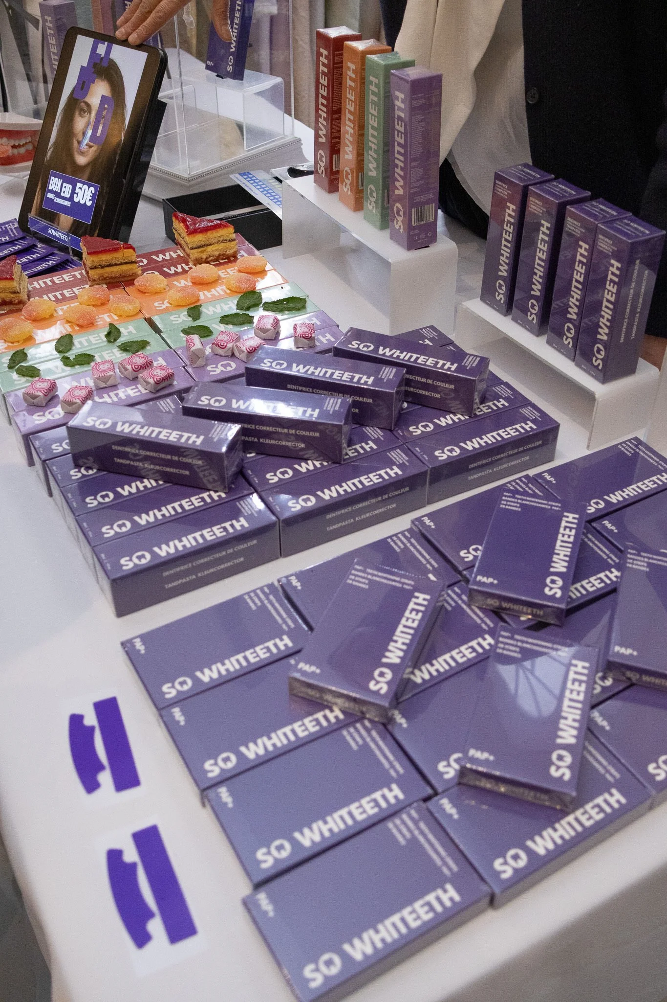 Tableau avec des boîtes de dentifrice SO WHITEETH, des tranches de gâteau, des macarons et des feuilles de menthe.