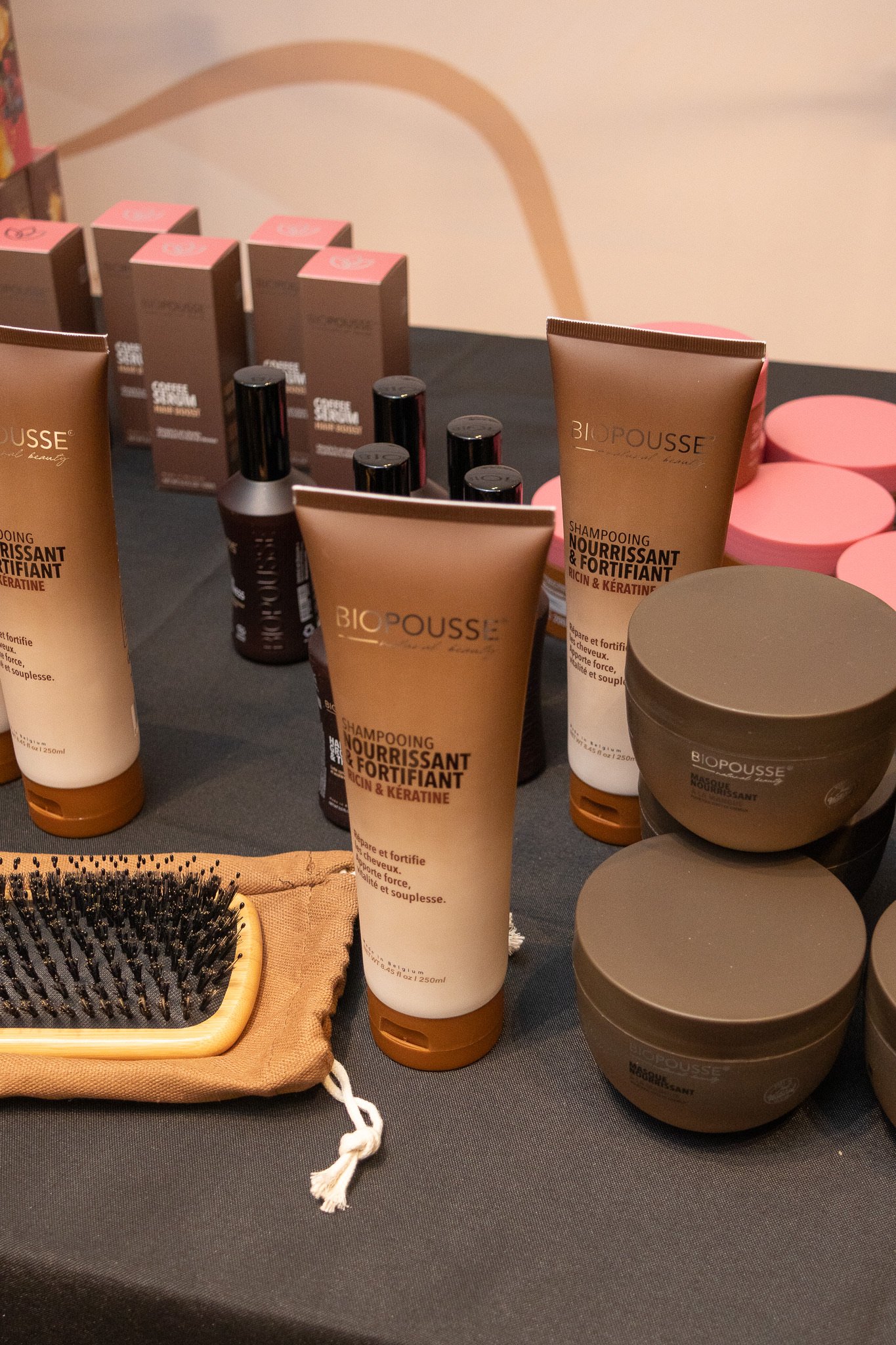 Produits capillaires Biopousse, shampoing nourrissant et fortifiant, masques et huiles, avec brosse à cheveux en bois naturel, sur une table noire
