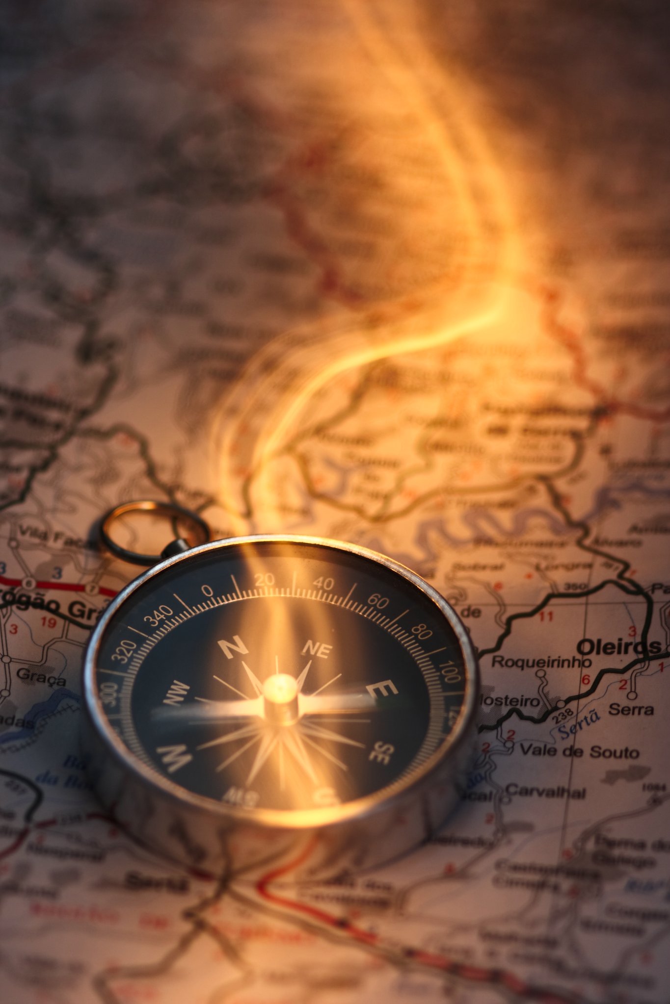 A compass resting on a map showing a winding route, with warm light reflecting off the compass and creating a glowing effect.