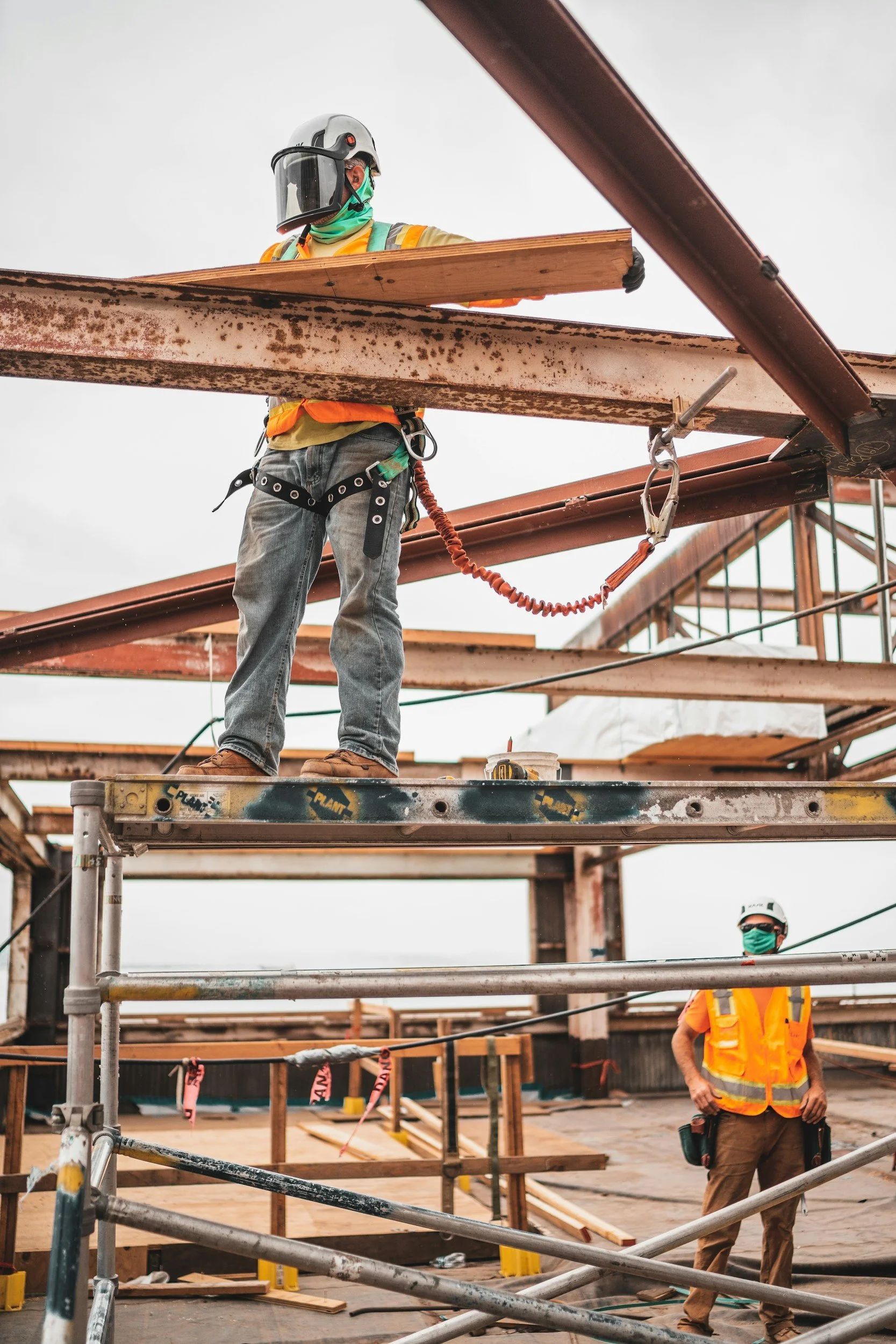 Construction workers on a building site wearing safety gear, with scaffolding and construction materials around.