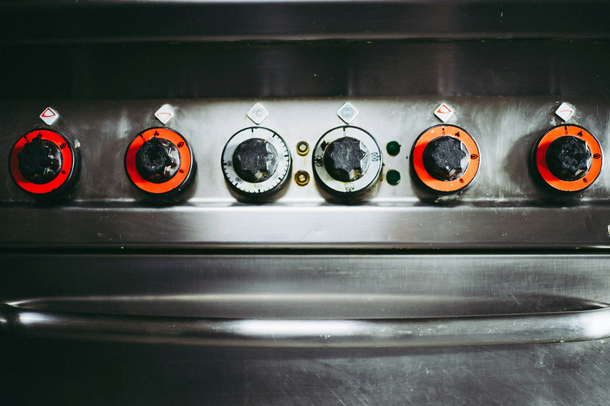 Close-up of a stove with five black control knobs, some with orange rings, and a few small indicator lights.