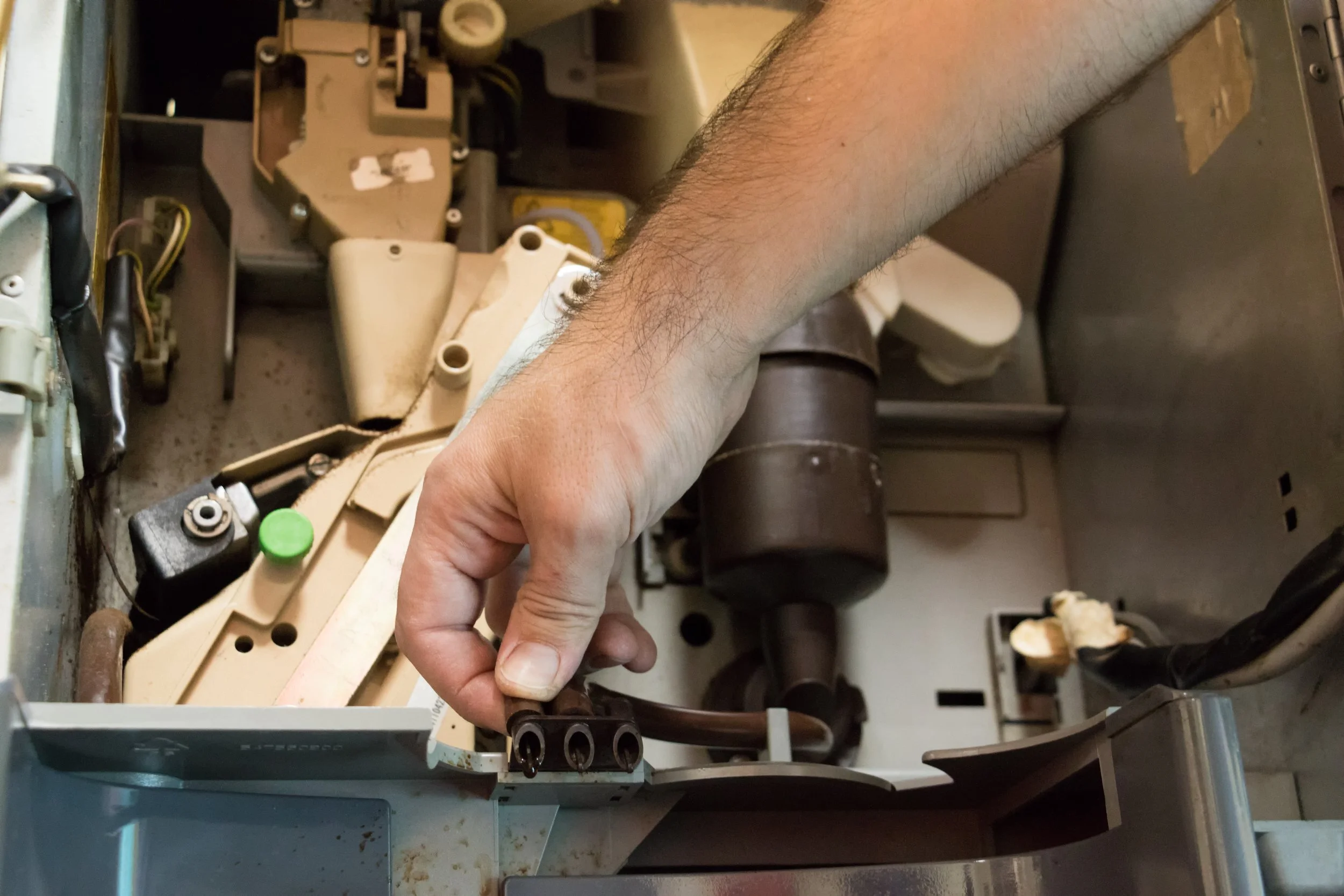 A person using their right hand to assemble a device inside a metal enclosure with various electronic components, wires, ducts, and a label with a barcode.