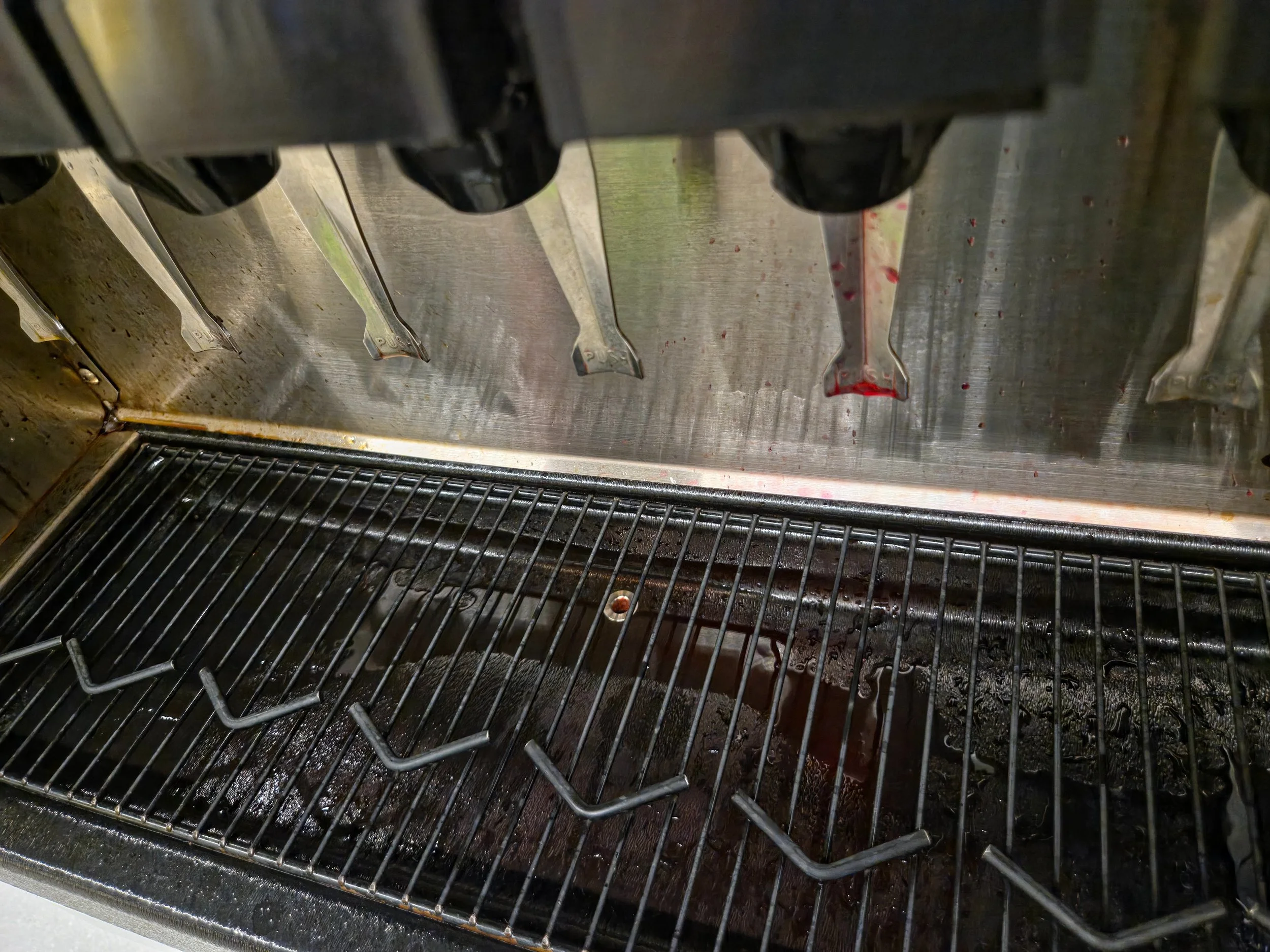 Interior view of a stainless steel commercial microwave oven with metal trays and some red sauce stains.