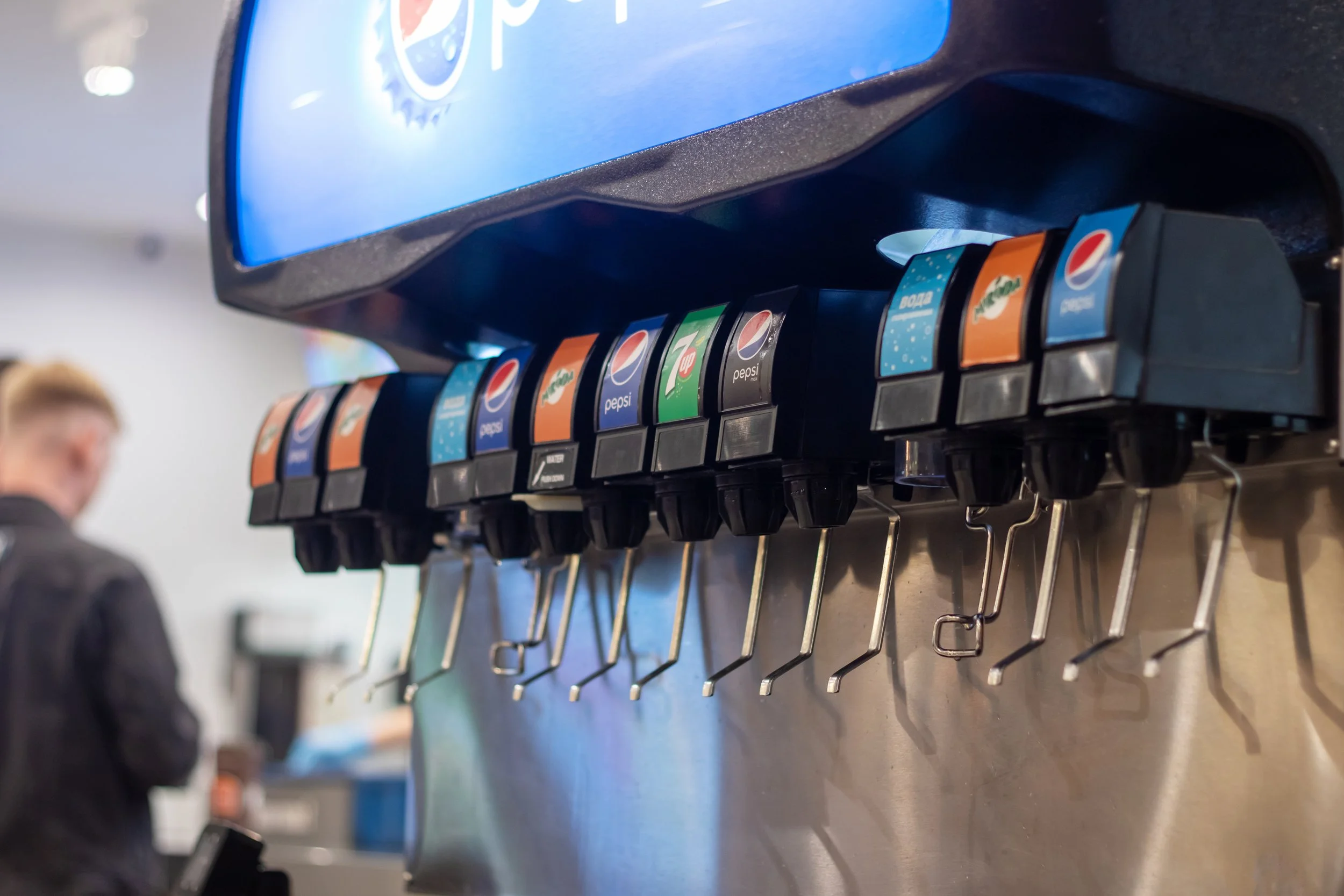 Close-up of a soda fountain machine with multiple Pepsi, Mountain Dew, 7UP, and Fanta drink options, and a blue screen on top.