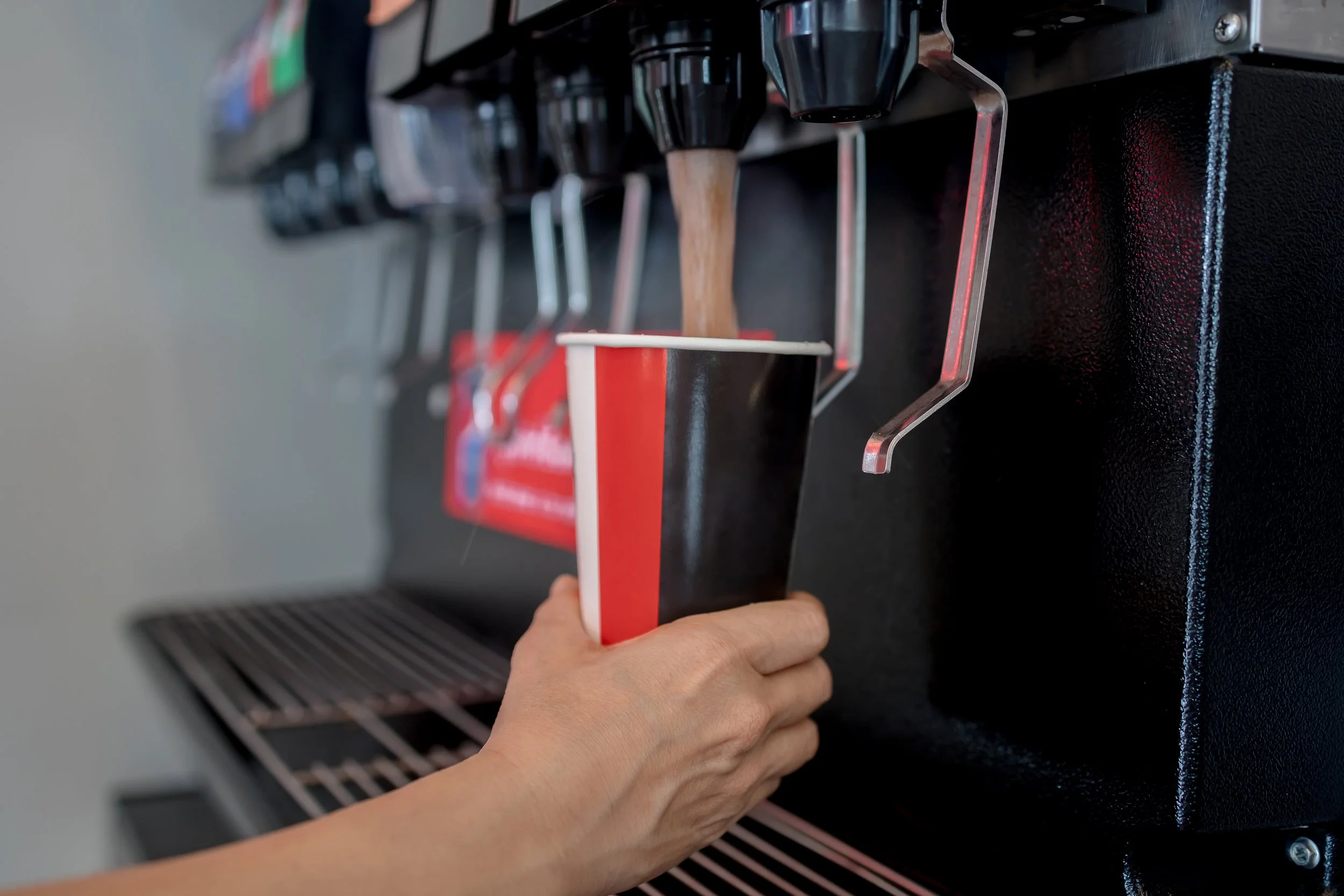 Person holding a paper cup of coffee under a coffee machine spout, ready to be filled.