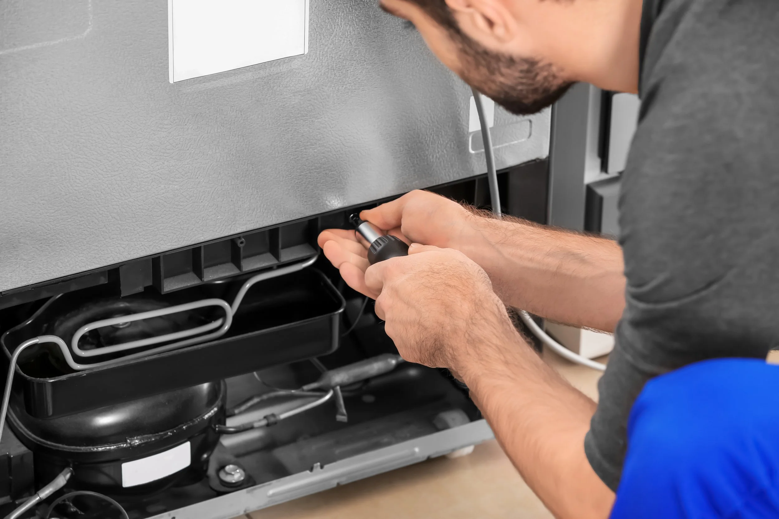 A technician using a screwdriver to repair a dishwasher in a kitchen.