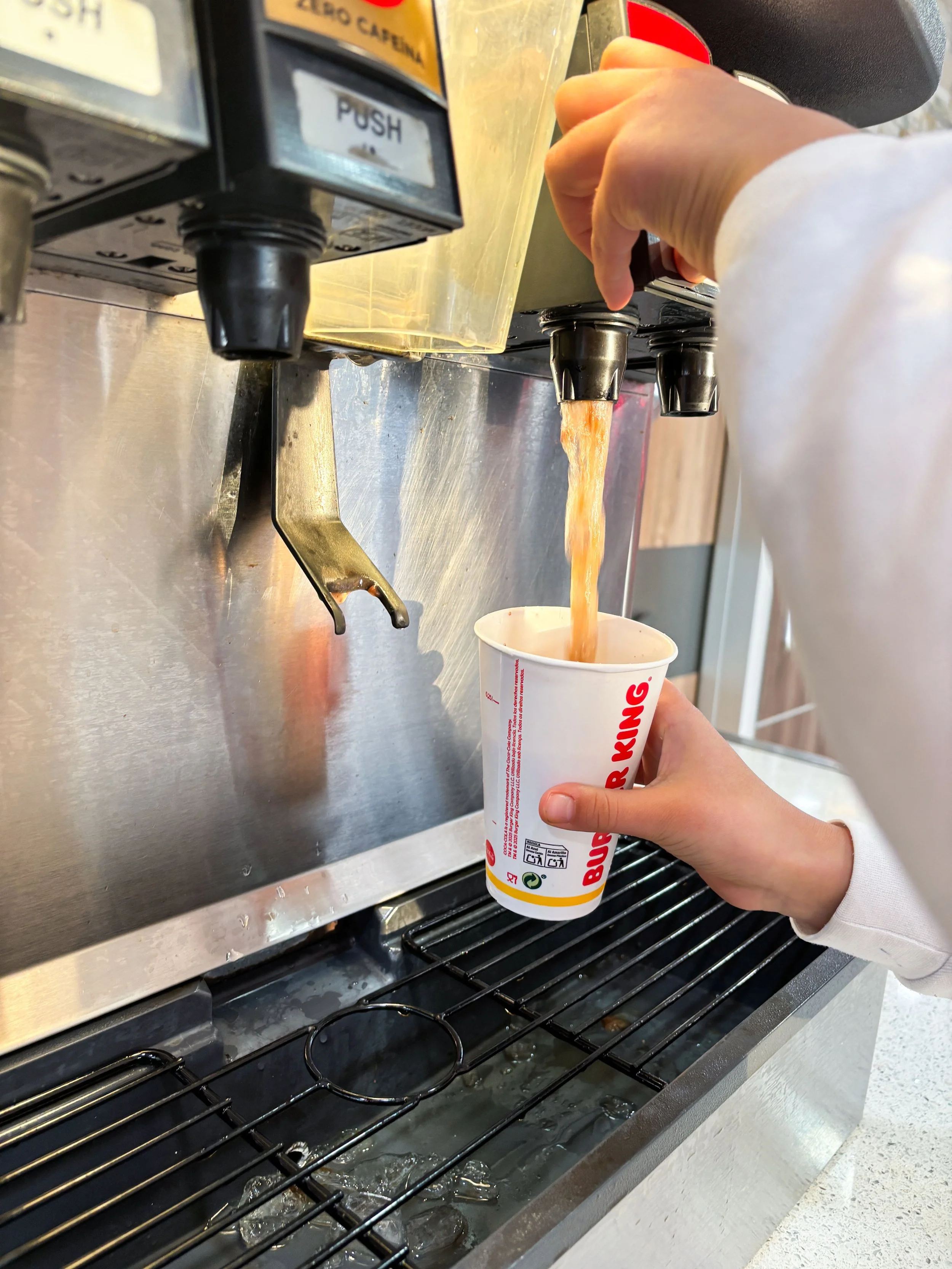 A person using a soda fountain to pour a soft drink into a cup at a fast food restaurant.