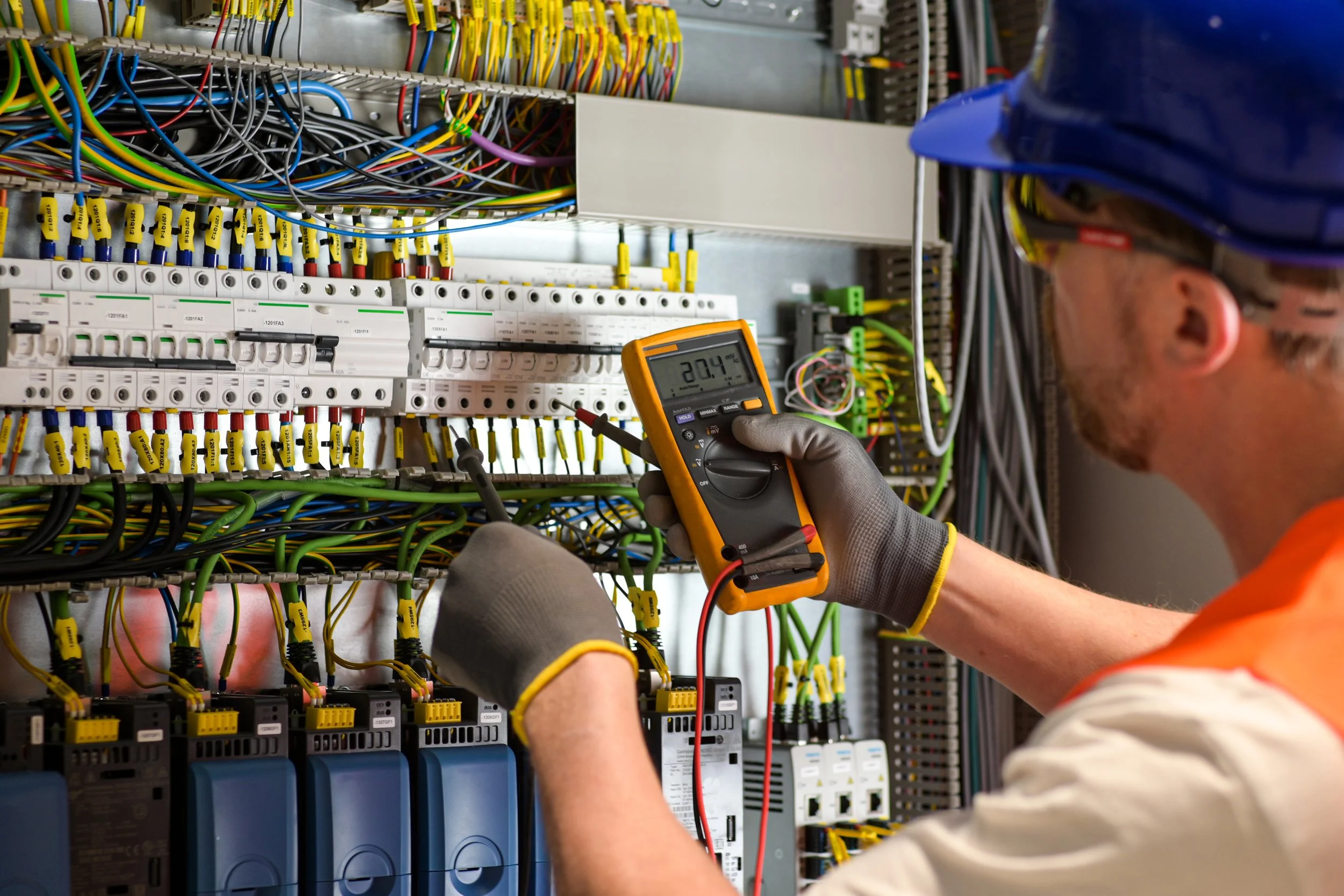 Technician testing electrical control panel with multimeter.