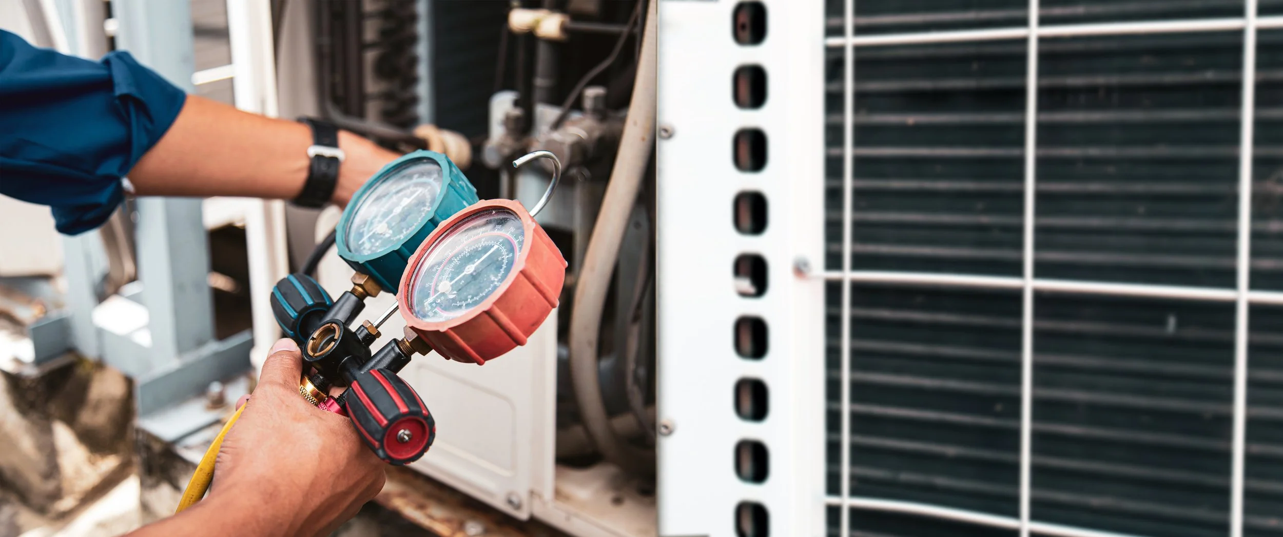 Technician checking air conditioning system with gauges and hoses in an industrial or commercial unit.