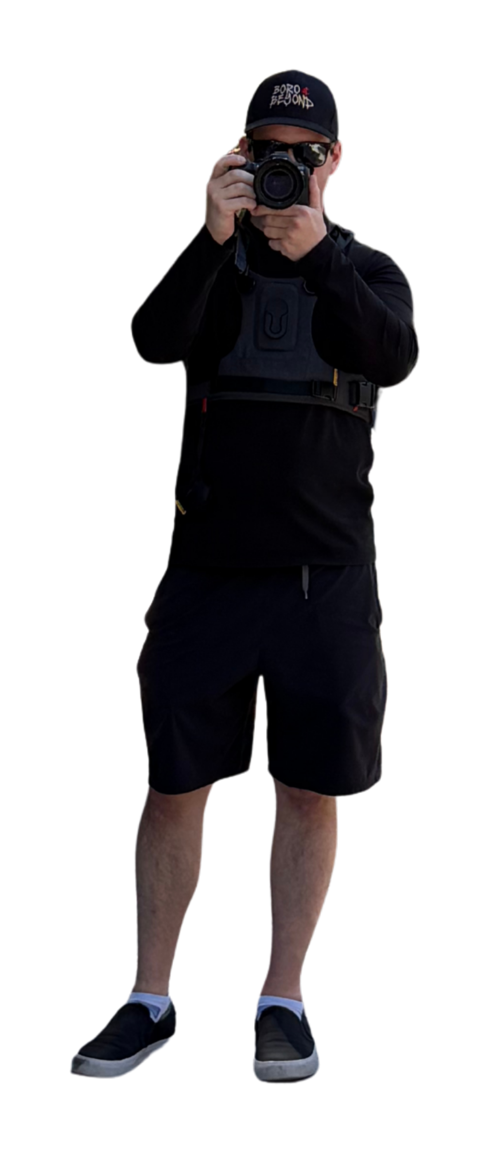 Man in black athletic wear taking a photo with a camera, wearing a black cap, sunglasses, and a camera strap.