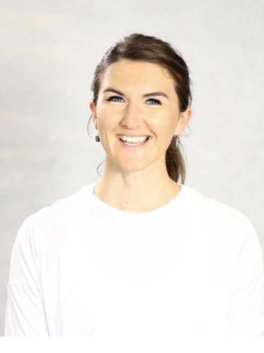 A woman with brown hair tied back, smiling, wearing a white top against a plain light background.