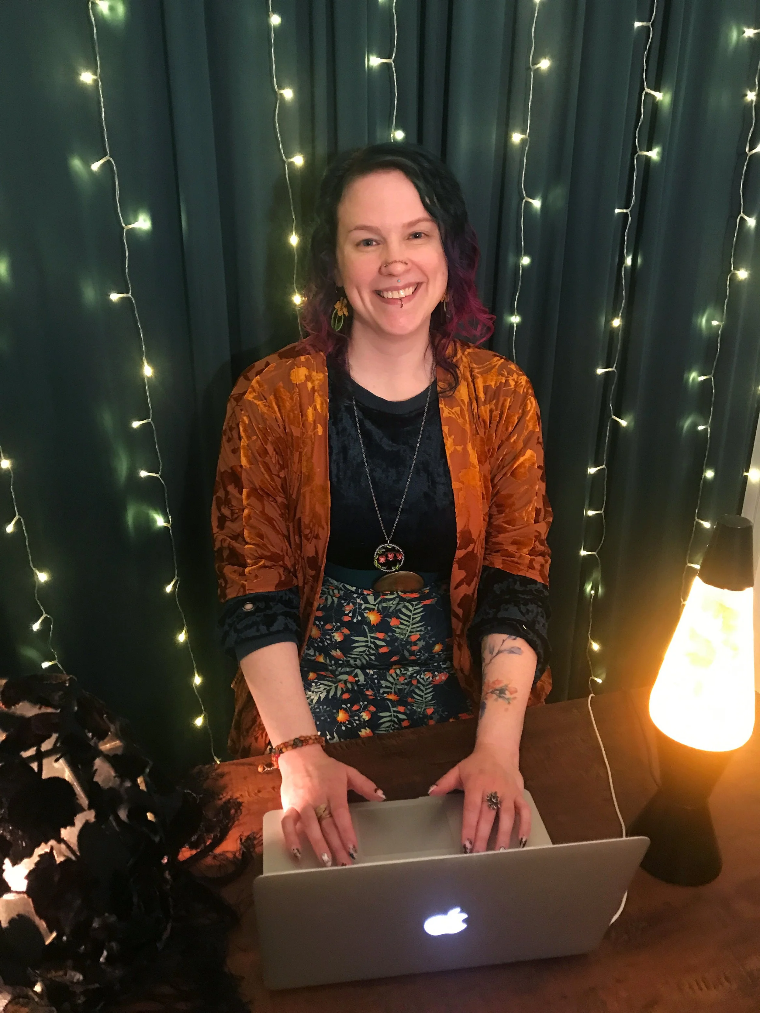 Picture of Bonnie, a smiling woman with shoulder length green and pink hair sitting at a laptop.