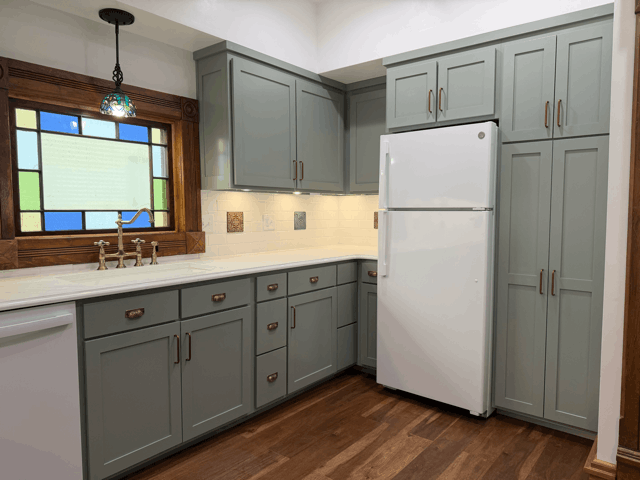  Custom kitchen cabinetry in soft green with white countertops, pantry storage, and refrigerator wall in remodeled historic home. 