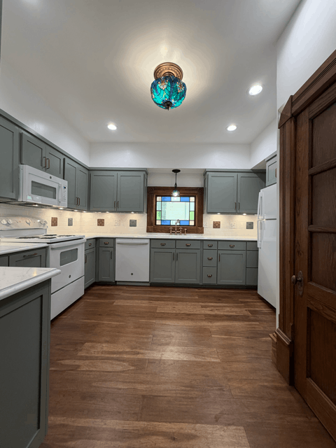  Wide view of remodeled Victorian kitchen with custom cabinets, wood flooring, modern appliances, and updated lighting layout. 