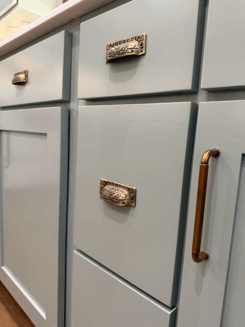  Custom kitchen cabinet drawers with antique brass hardware and soft green painted finish in remodeled kitchen. 