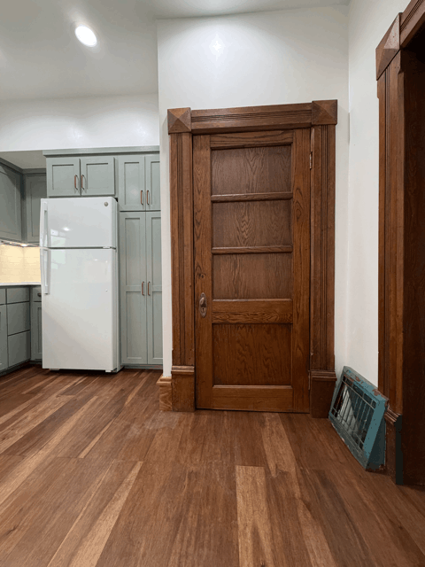  Historic home interior with refinished wood door, wood trim, and new flooring connecting kitchen remodel space. 