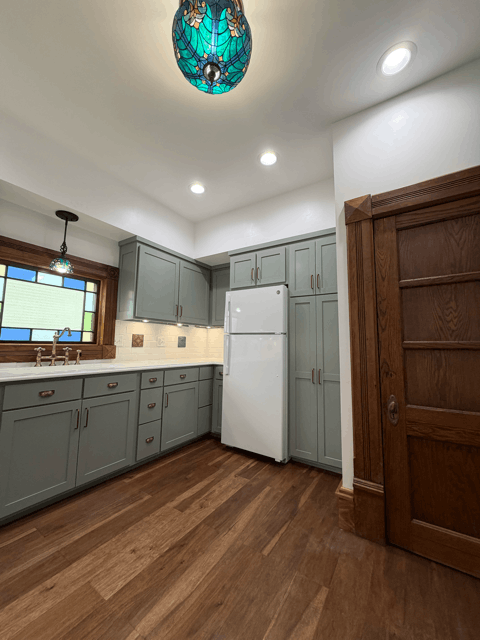 Corner view of remodeled kitchen with custom cabinetry, refrigerator wall, wood flooring, and preserved historic trim details.