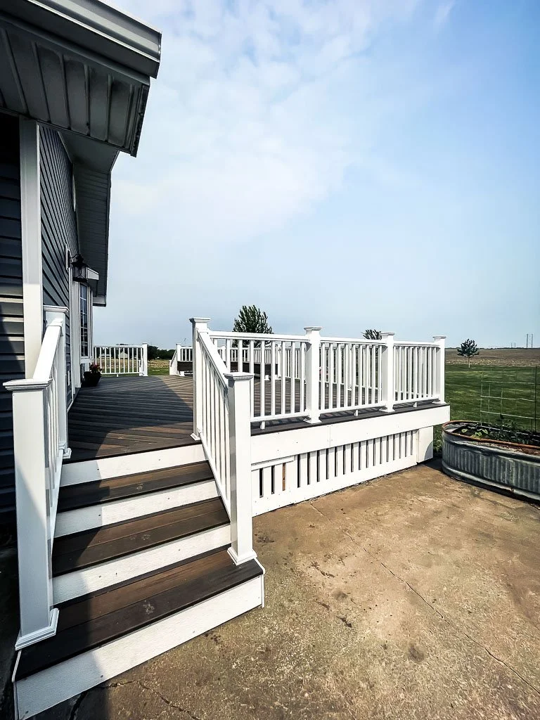 Newly constructed elevated deck with white railing and stairs overlooking the countryside. Built by Rural Renovation to enhance outdoor living space and curb appeal in Hopkins, Missouri.