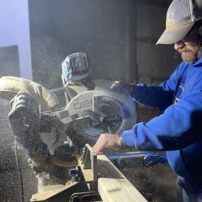 Rural Renovation craftsman cutting wood for a custom trim installation during a home restoration project in Pickering, Missouri. Precision carpentry and dust in motion capture the craftsmanship behind the work.