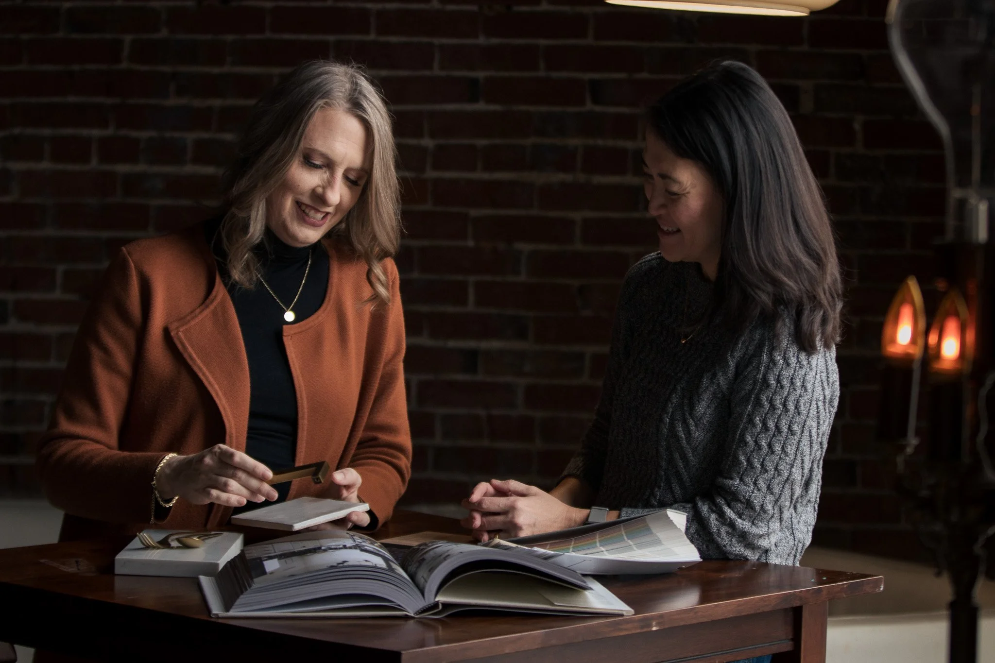 Amber Parker smiling and talking to a client in front of a brick wall showing her tile options for her home renewal.