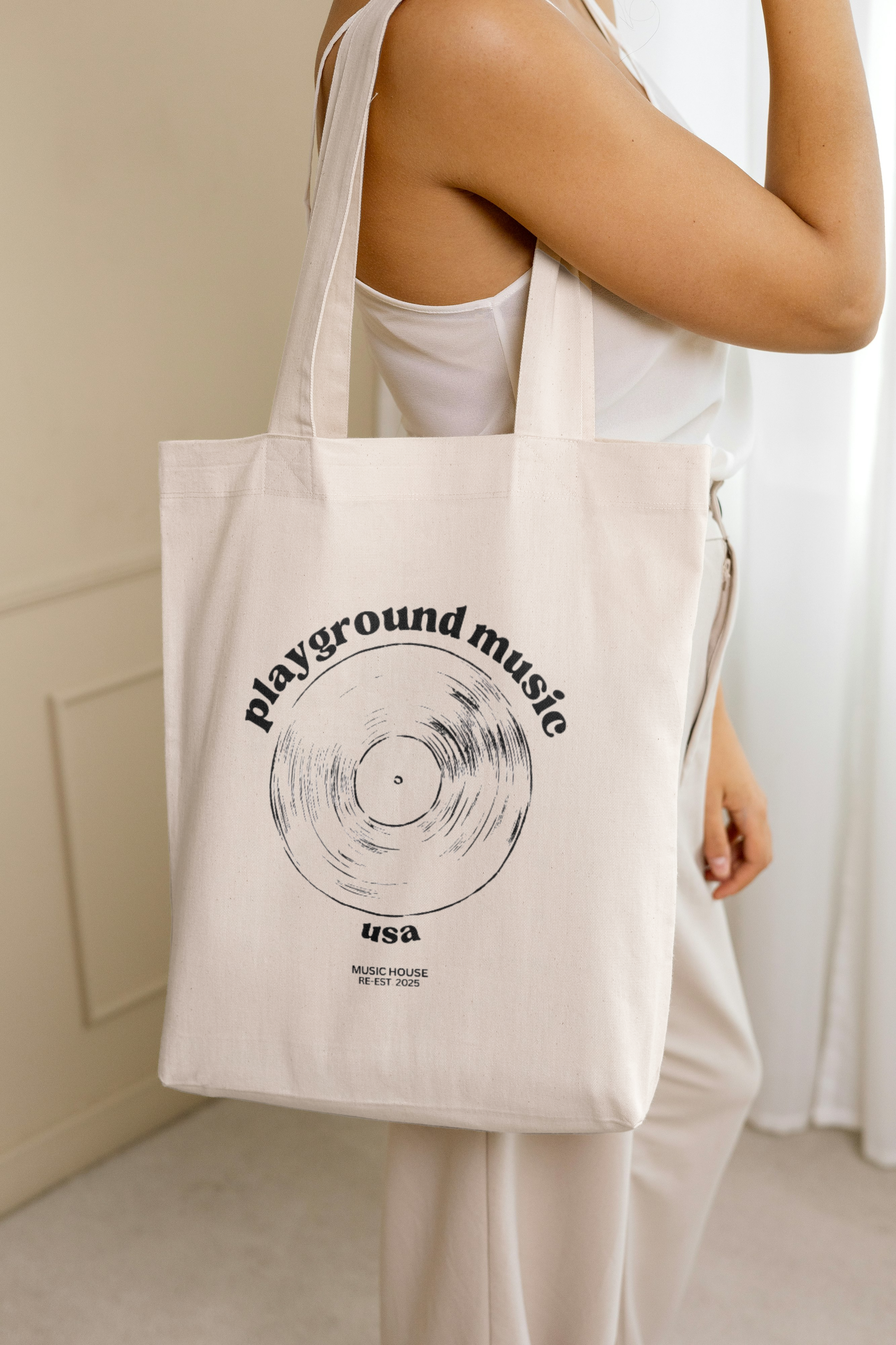Person holding a beige tote bag with 'playground music usa' written on it and a vinyl record graphic.
