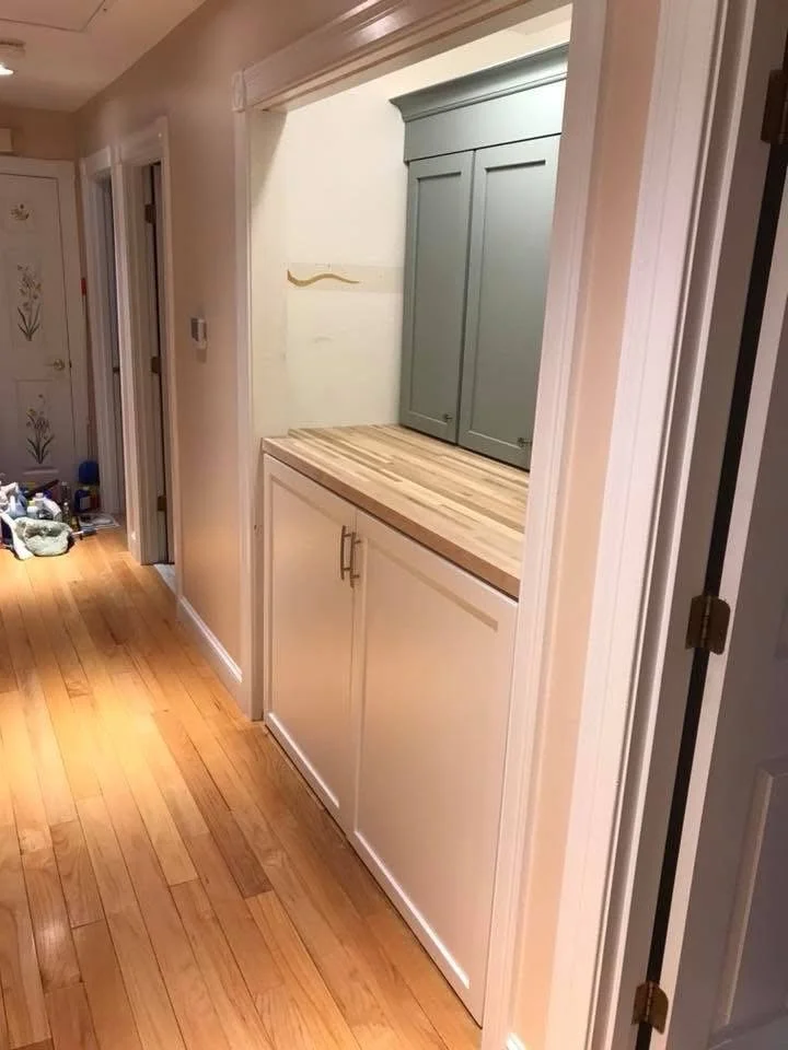 A built-in cabinet with a countertop in a hallway, with a green upper cabinet and a white lower cabinet, and a hardwood floor.