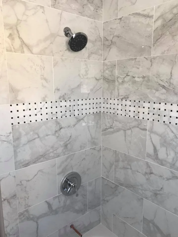 Corner of a marble-tiled shower with a round showerhead and a single handle valve.