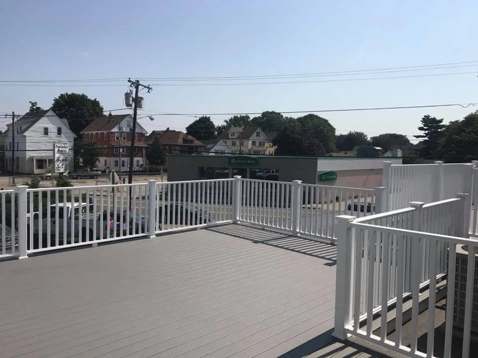 Empty outdoor deck with white railing overlooking a parking lot and a row of houses across the street.