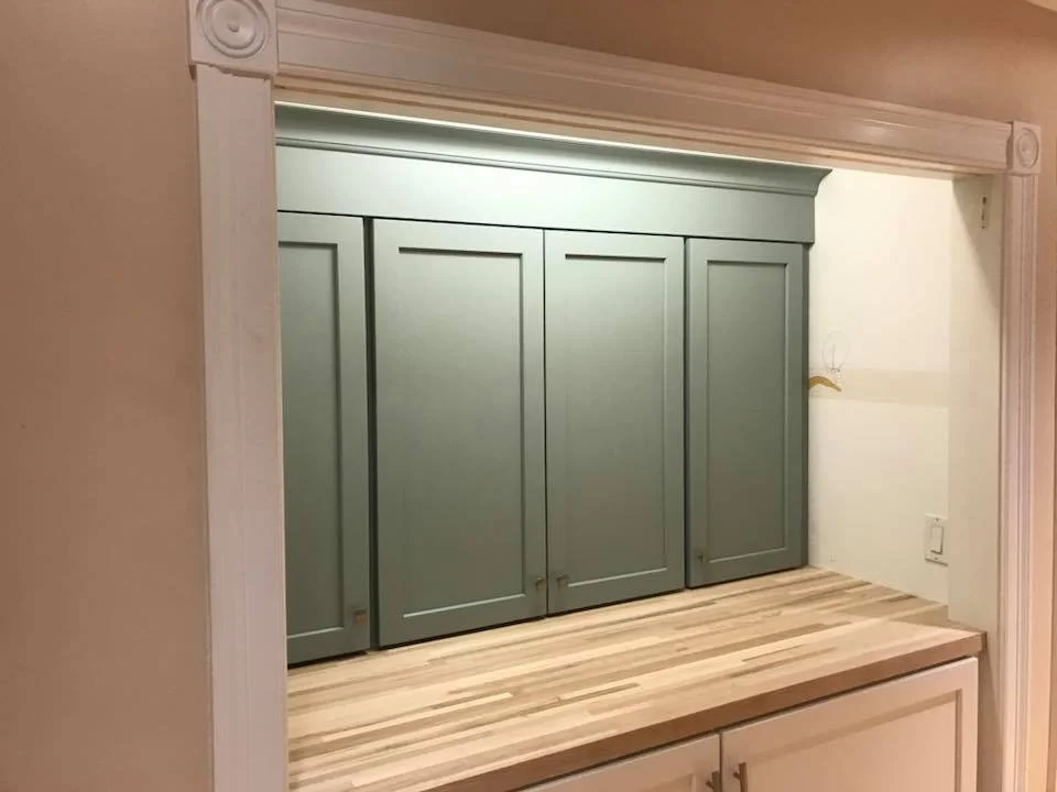 Close-up of a built-in kitchen cabinet with three mint green doors and brass handles, situated on a wooden countertop, framed by a white trim.