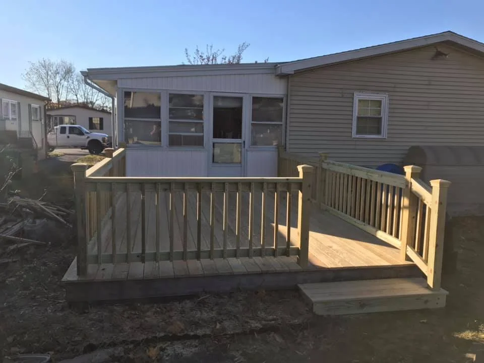 New wooden deck with railing attached to the back of a house, with stairs leading down to the yard, and a screened porch area.