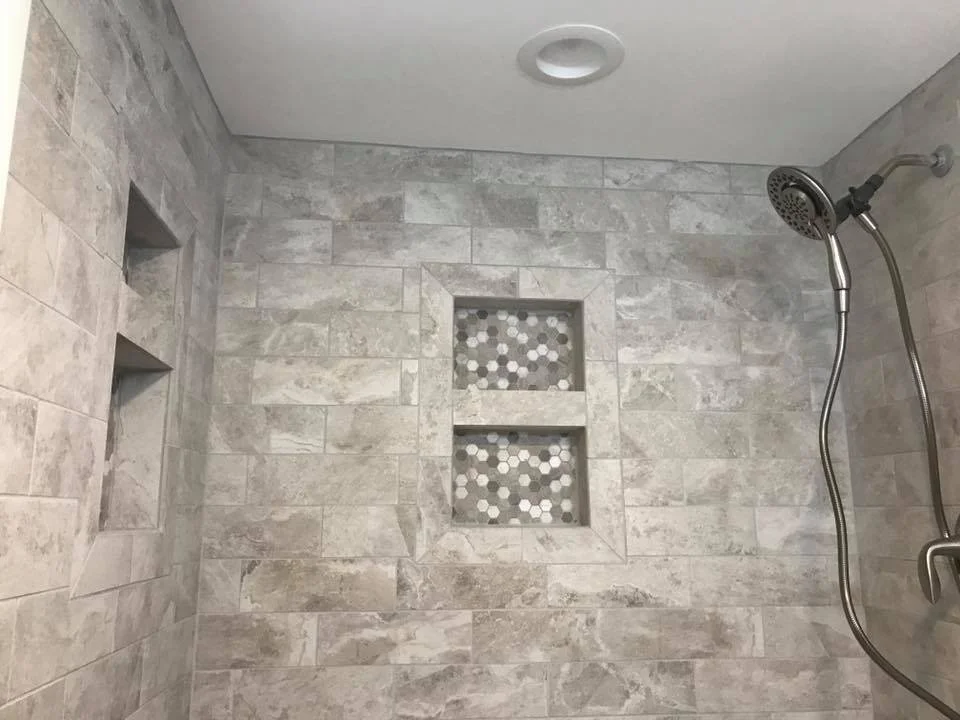 Shower with gray stone tiles, built-in shelves, and a handheld showerhead.