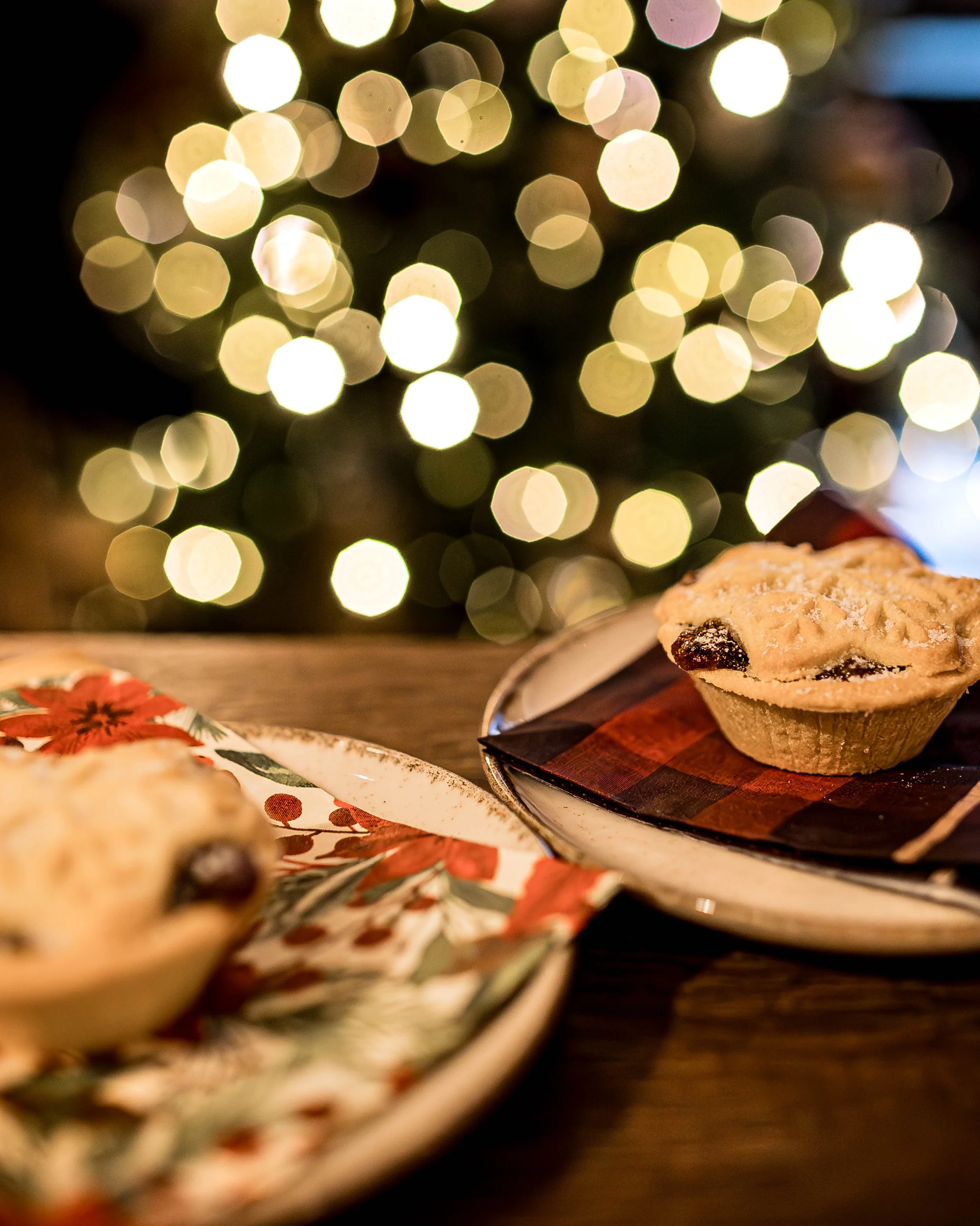 A plate with a muffin and another dessert on a festive table, with blurred Christmas lights in the background creating a warm holiday atmosphere.