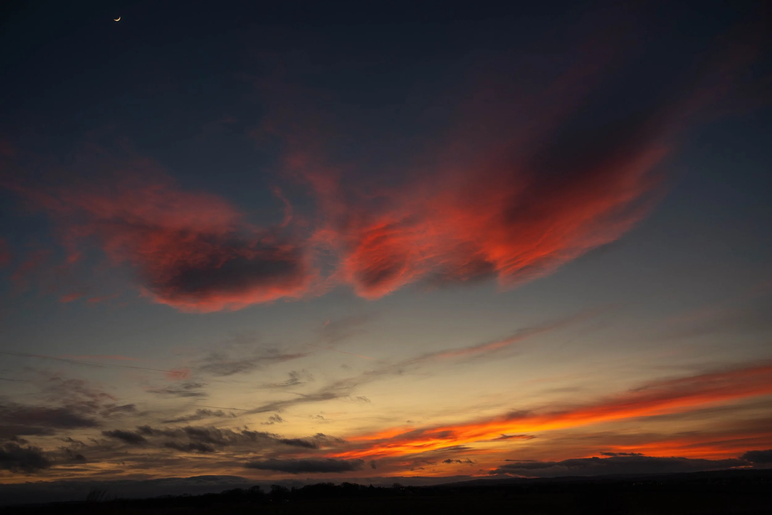 Colorful sunset sky with orange, pink, and purple clouds, and a crescent moon in the distance.