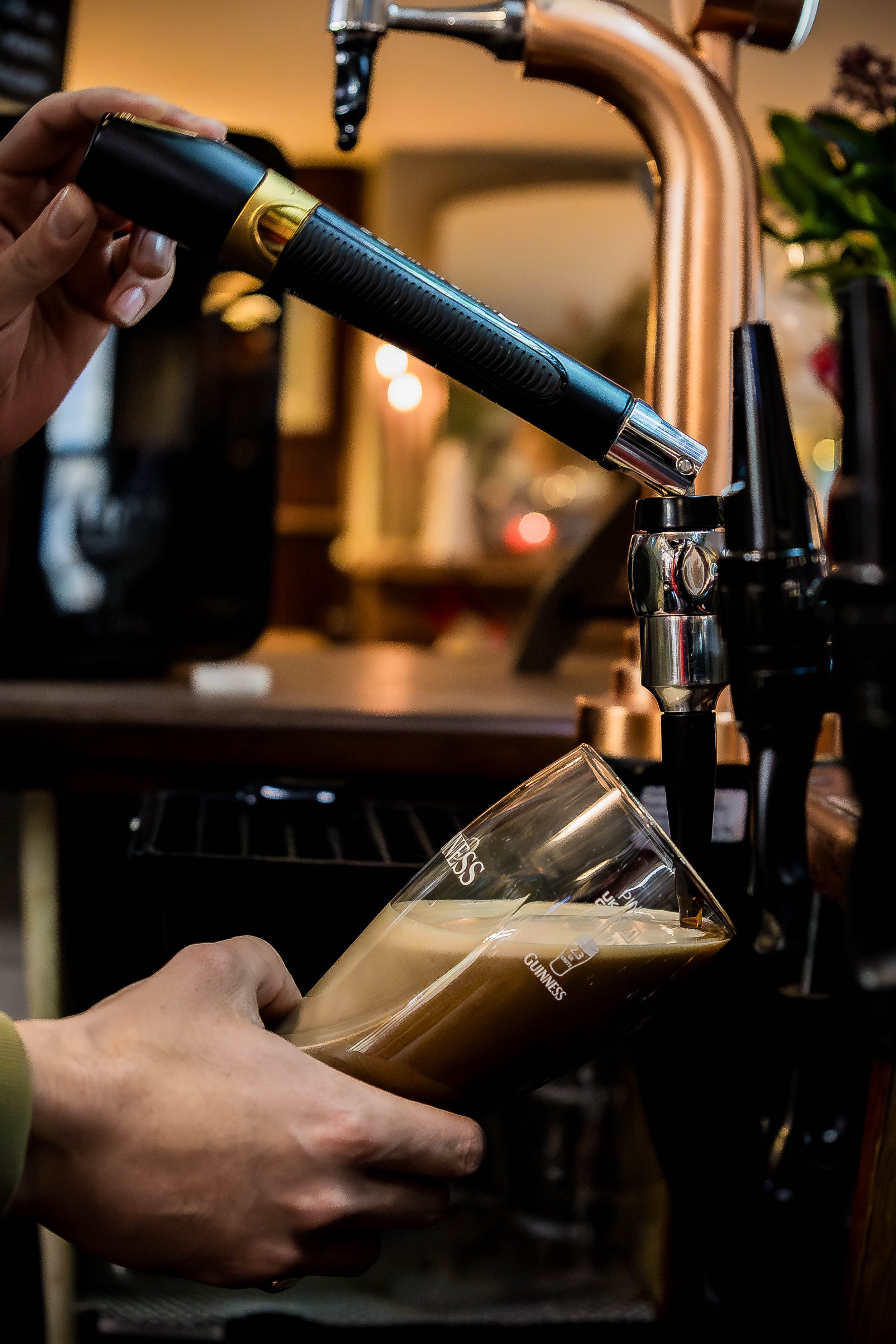 A person is pouring a dark beer from a tap into a pint glass in a bar or pub setting.