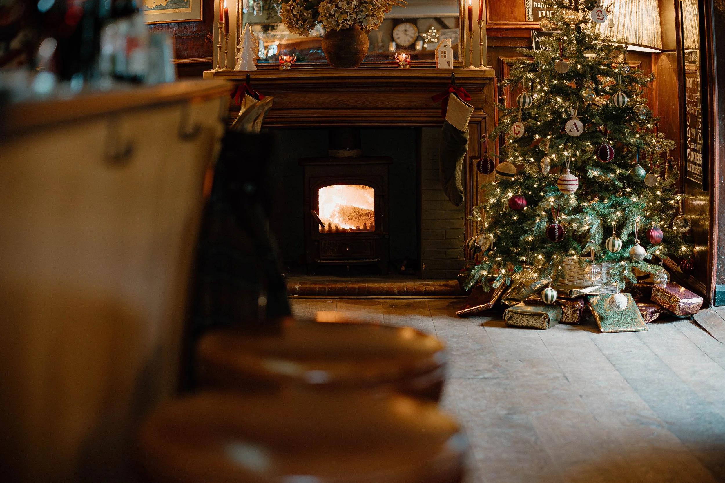 Decorated Christmas tree with wrapped presents underneath, in a cozy room with a lit fireplace and holiday decorations.