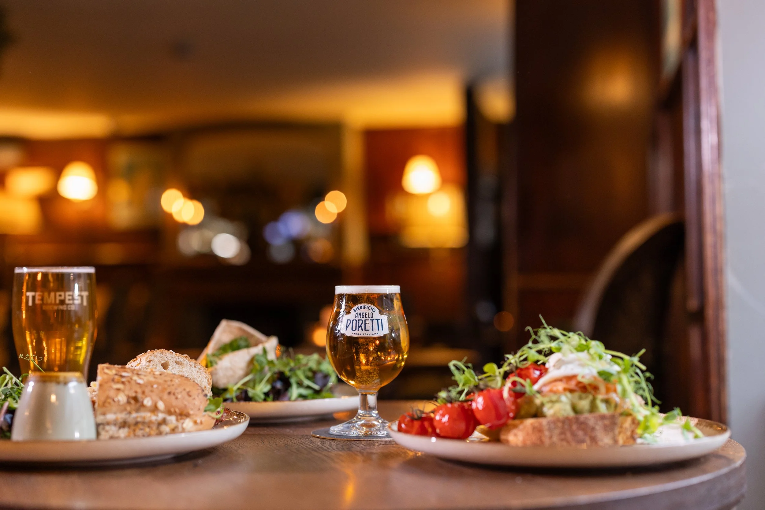 A table with plates of salad, bread, and glasses of beer in a warmly lit restaurant.