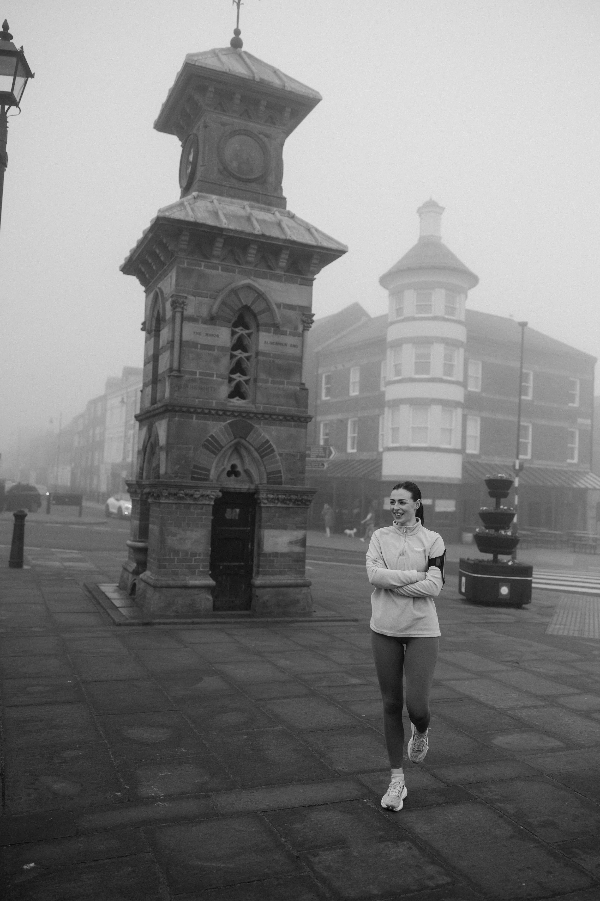 A woman jogging on a foggy street with historic buildings and a clock tower in the background, black and white photo.