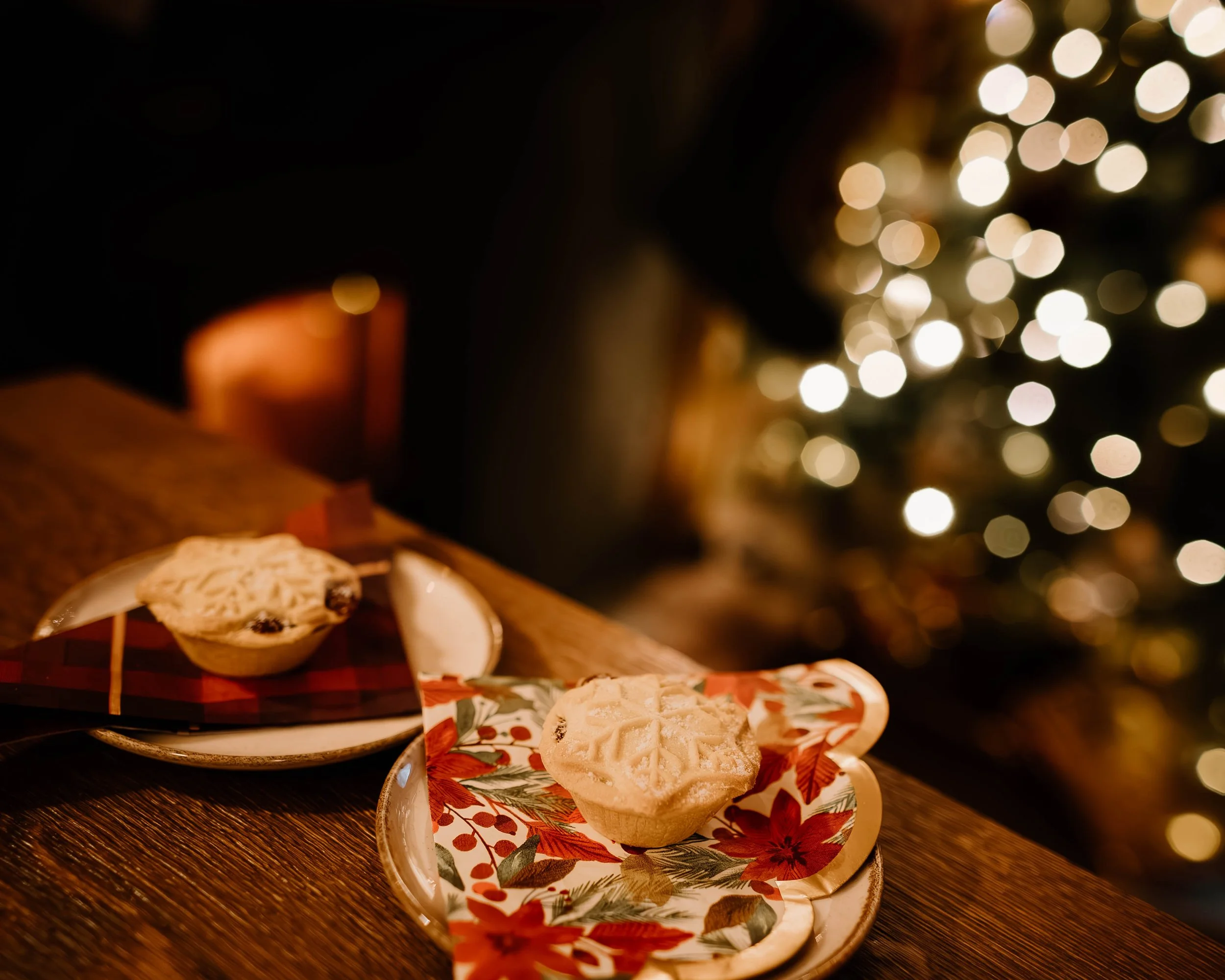 Two holiday-themed dessert cups on decorative plates with a Christmas tree and blurred white lights in the background.