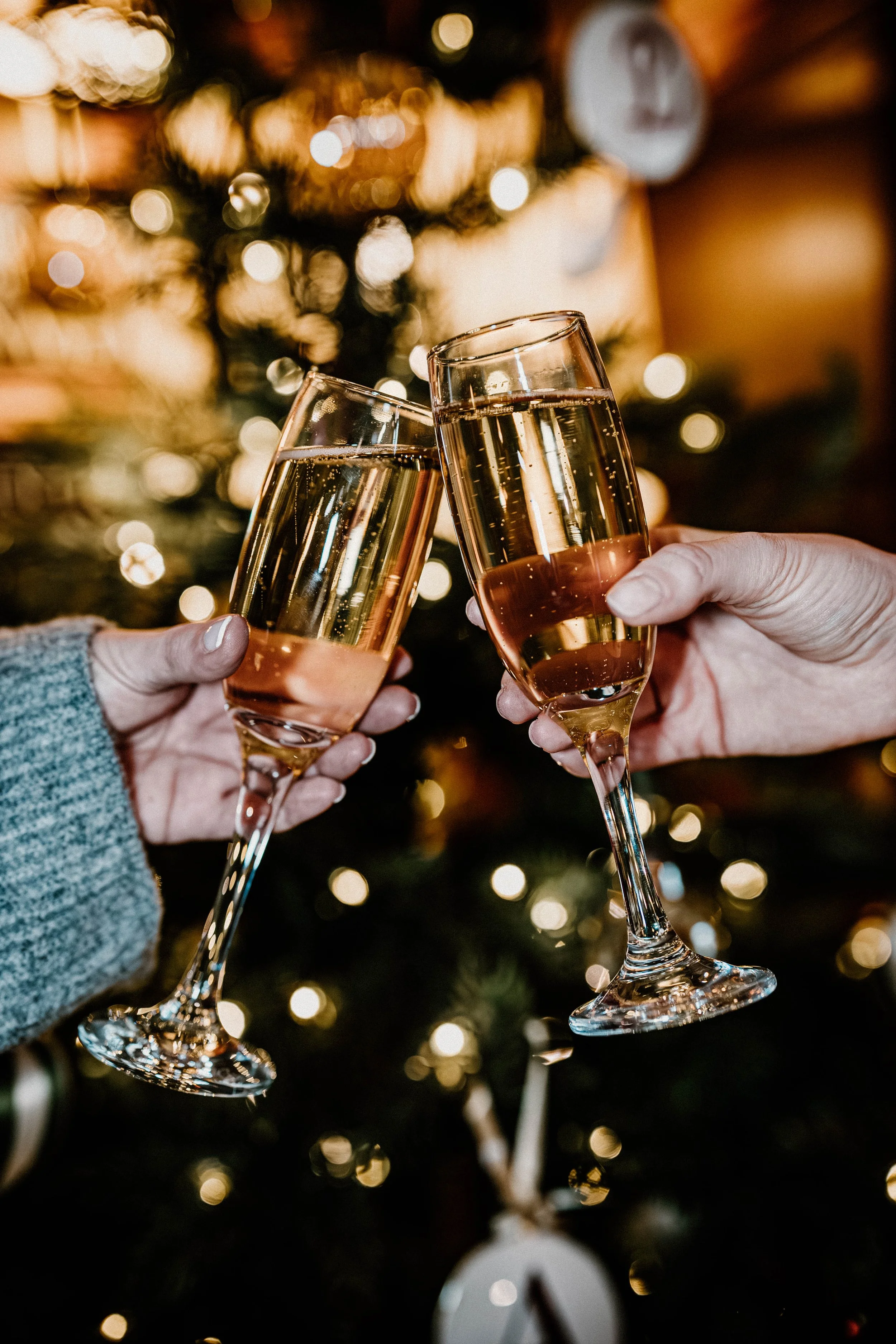 Two people clinking glasses of champagne in front of a decorated Christmas tree.