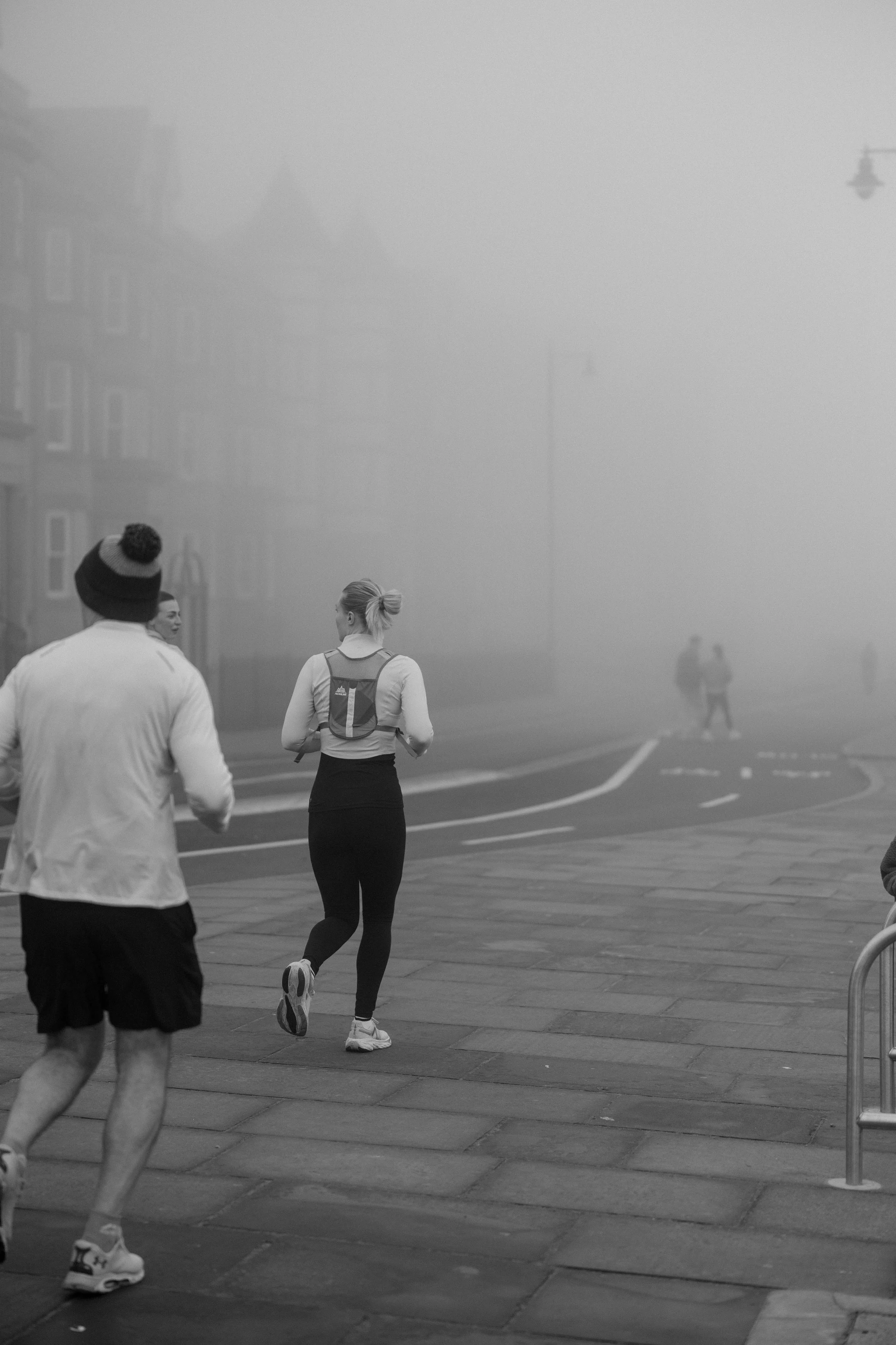 People jogging on a foggy street.
