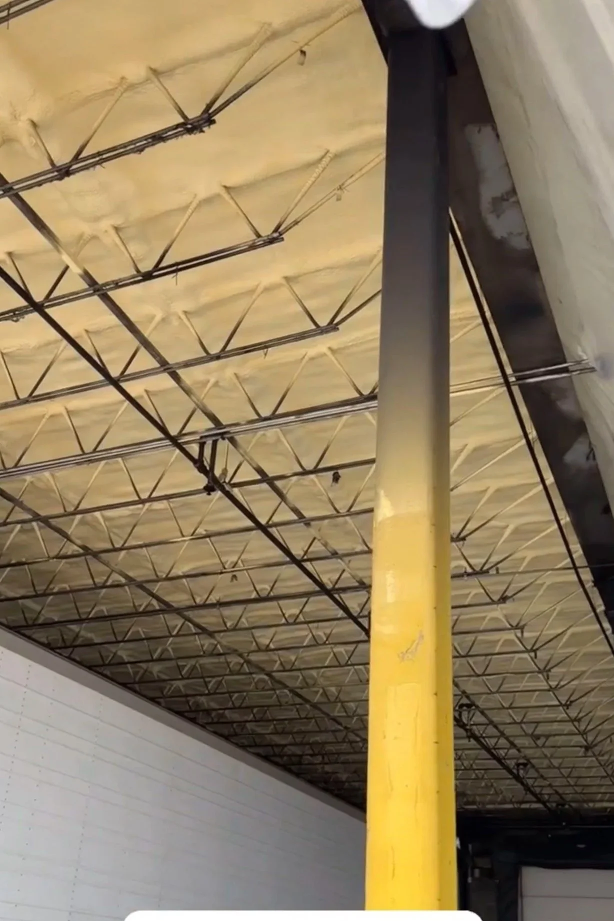 Interior of a warehouse with a yellow support pole, a large white truck trailer, and exposed ceiling insulation and metal beams, at Richelieu Foods, Inc.